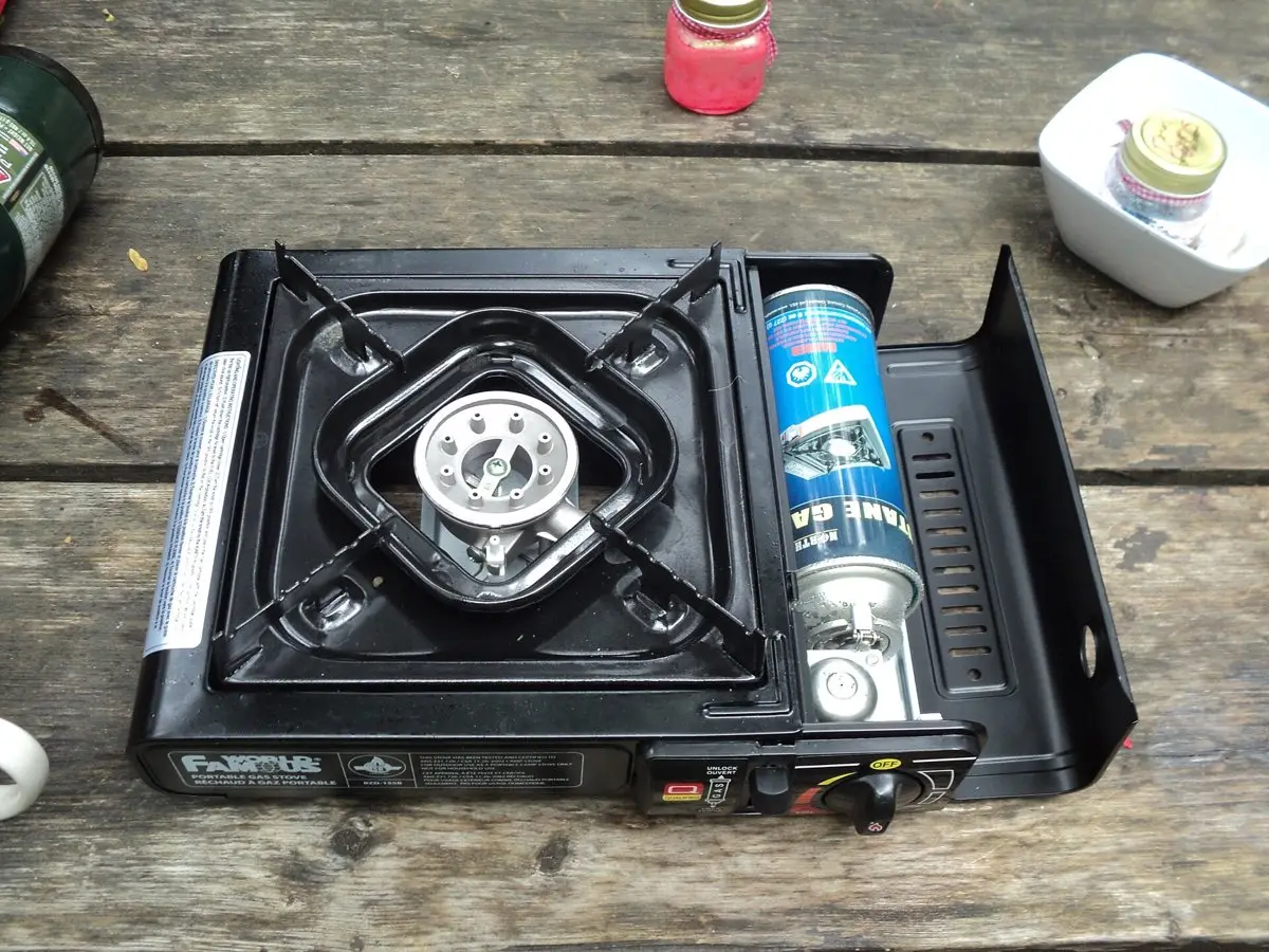 A portable butane camp stove with a gas canister fitted, sitting on a wooden picnic table